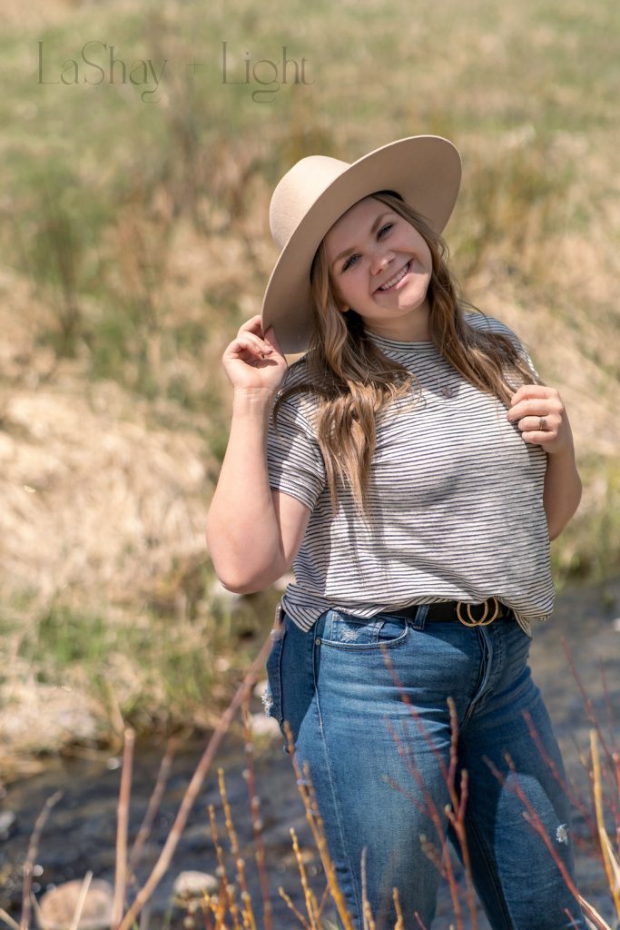 girl tilting hat and smiling by a creek 