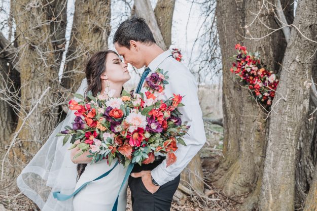bride and groom about to kiss in the woods with a colorful bouquet
