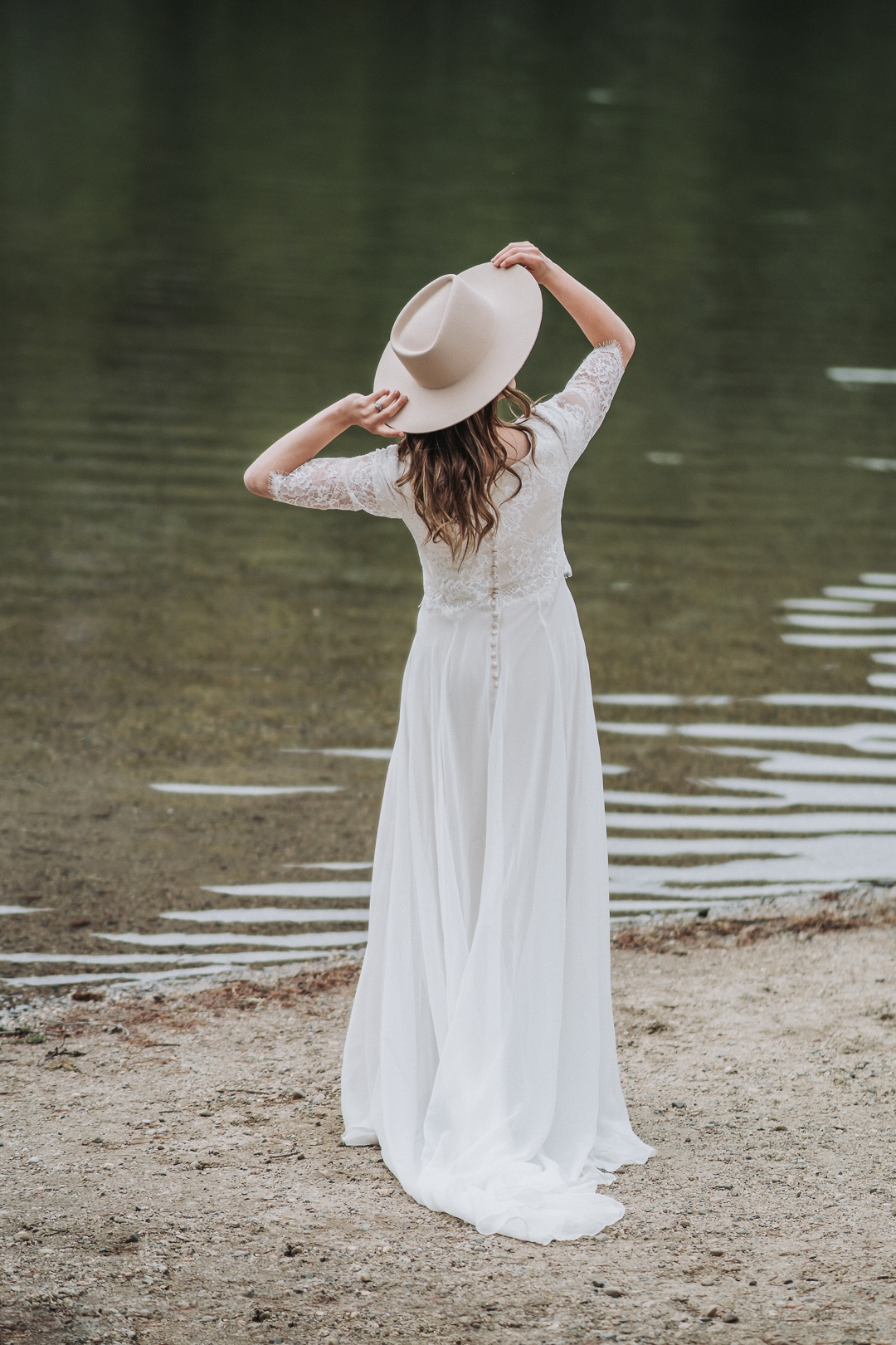 bride holding hat while looking into string lake